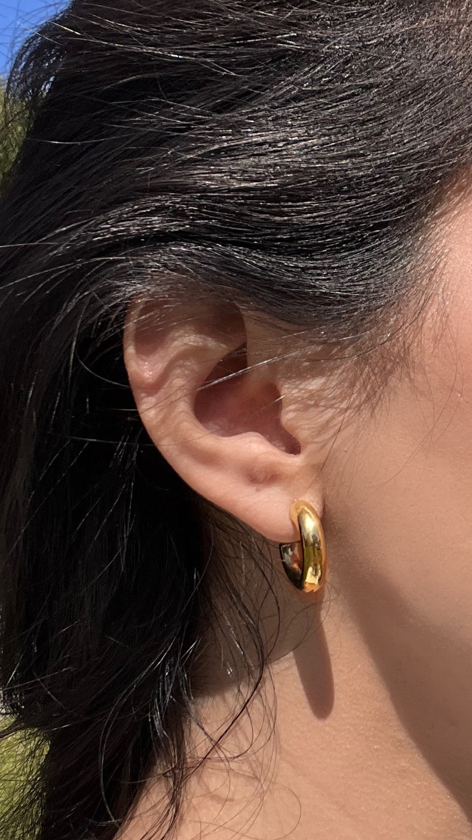 Woman wearing thick gold hoop earrings outdoors