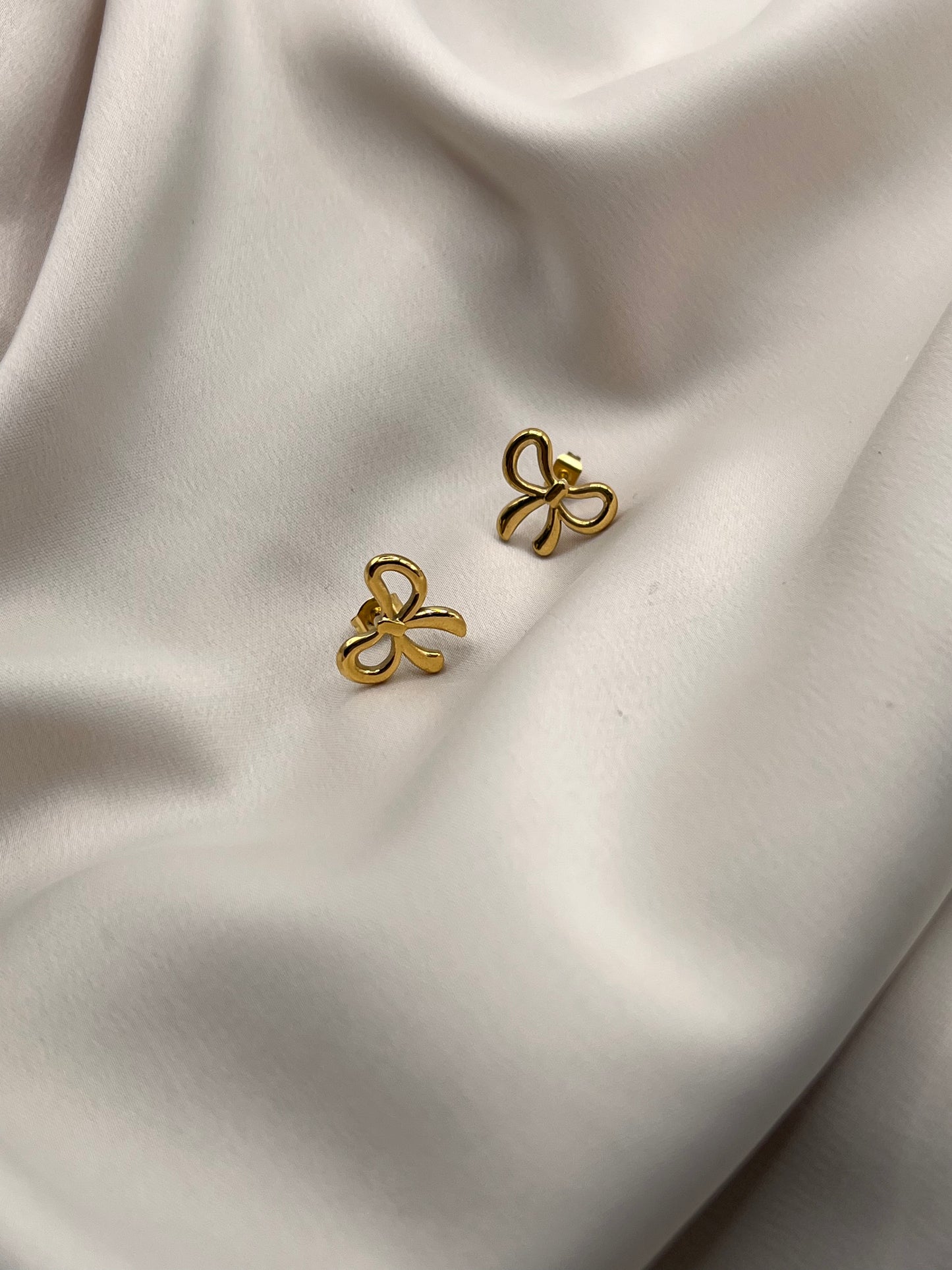 Dainty gold bow earrings on satin fabric