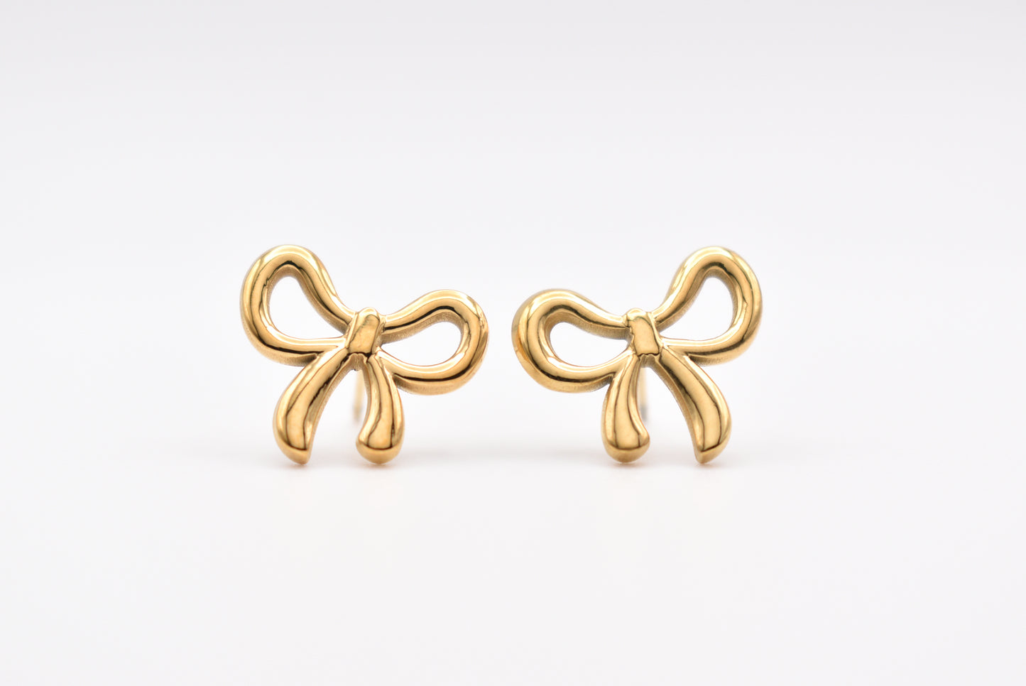 Gold bow-shaped stud earrings on white background