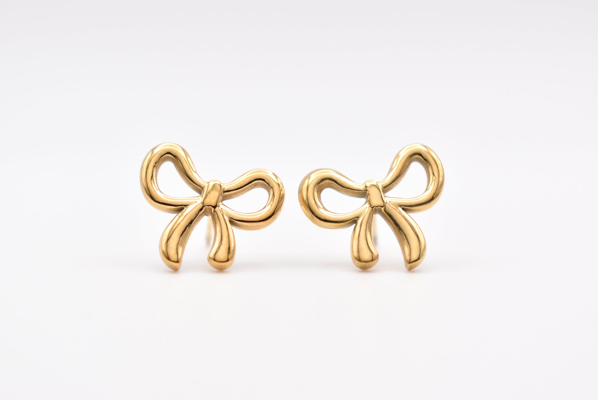 Gold bow-shaped stud earrings on white background